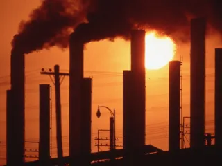 Silhouette of smokestacks at a U.S. Steel plant in Birmingham, Alabama, emitting dark smoke against a glowing orange sunset.